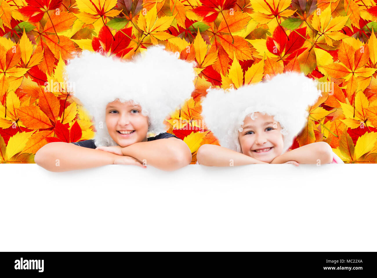 Sorridendo felice due giovani ragazze in parrucche bianche guardare fuori da il banner vuoto sullo sfondo di caduto foglie di autunno. Foto Stock