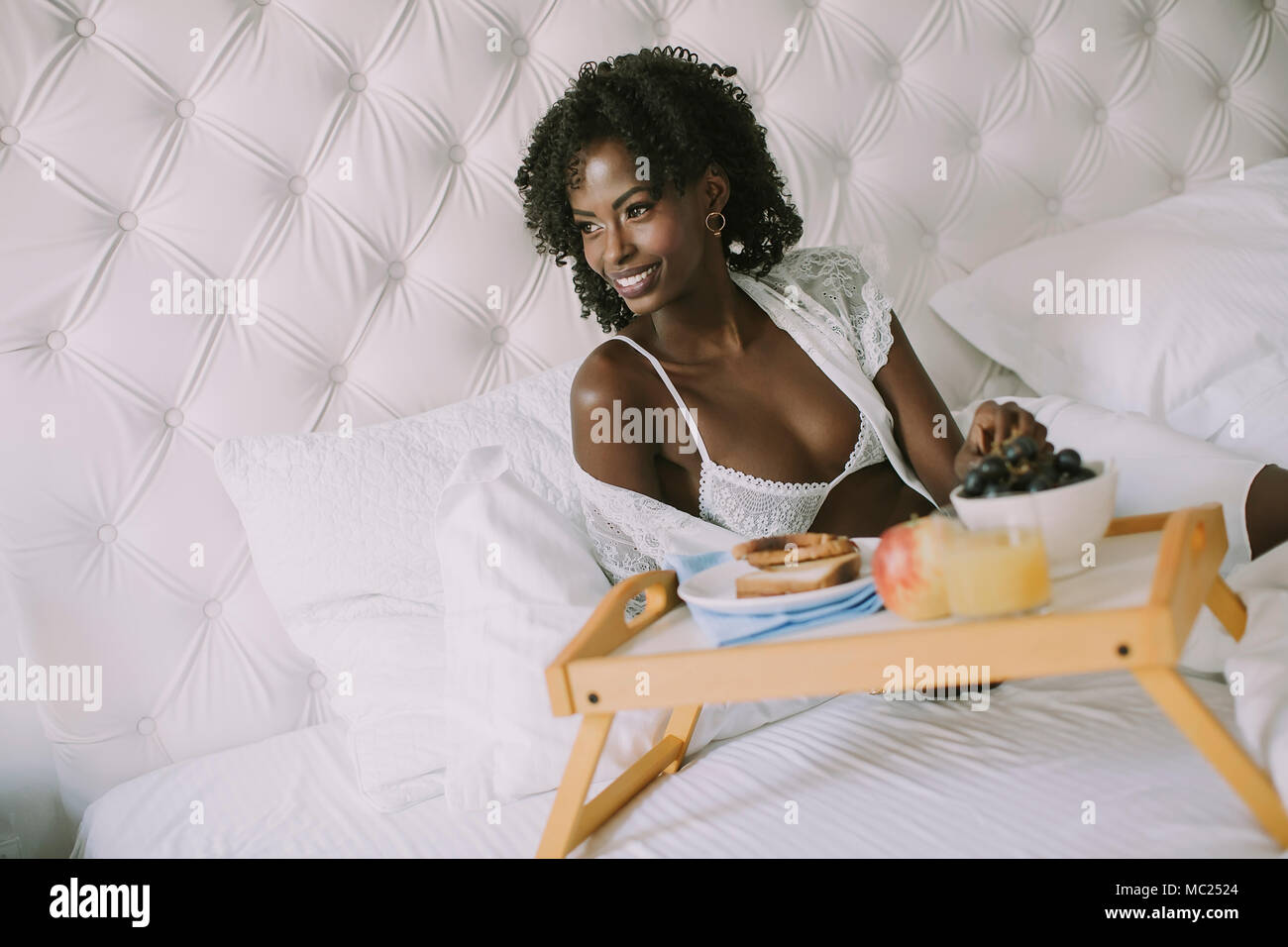 Sorridente giovane africano donna americana avente una rilassante colazione a letto a casa Foto Stock