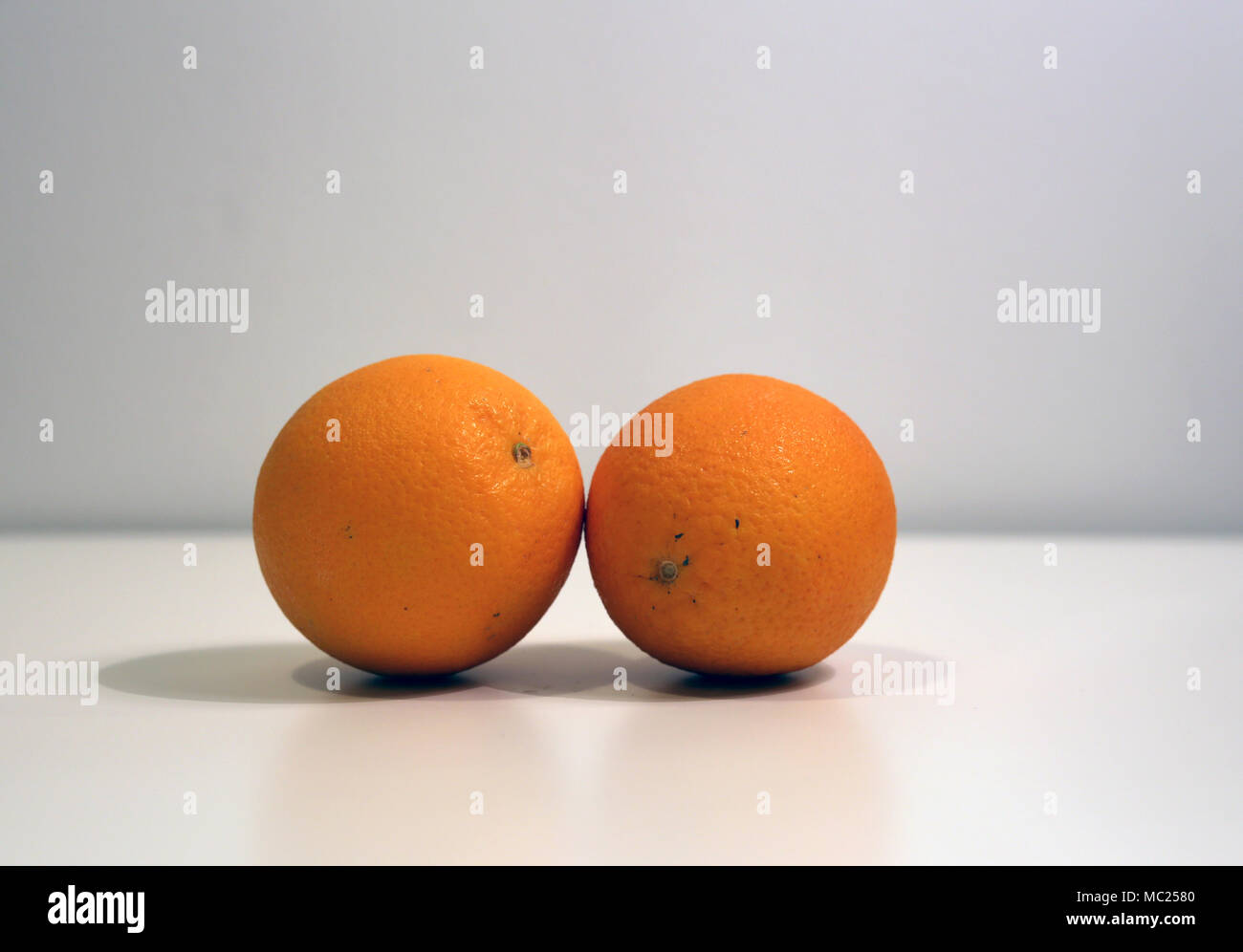 Due arance su una tavola appoggiata su ogni altra. Semplice e bel frutto vivono ancora con bianco / grigio. Foto Stock