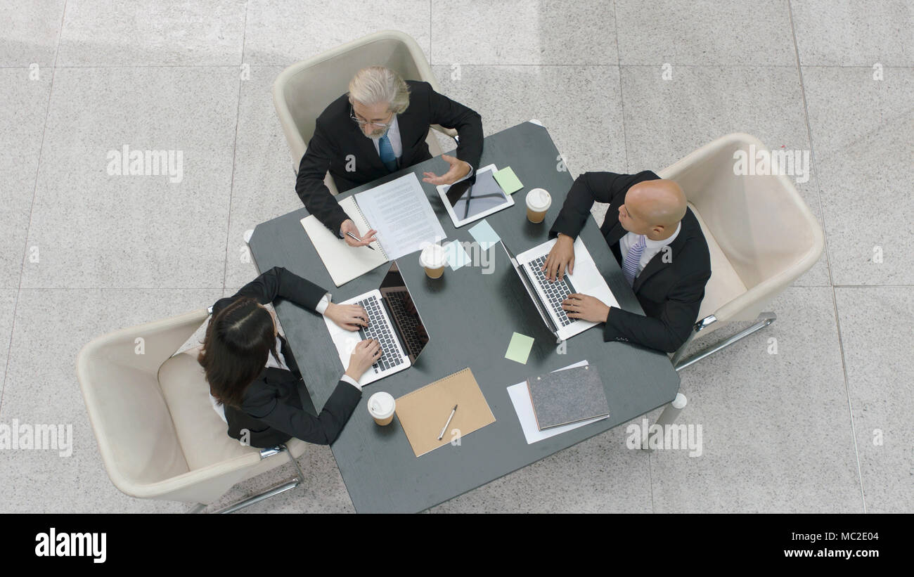 Angolo di alta vista di tre dirigenti aziendali incontro discutere di affari in ufficio moderno. Foto Stock
