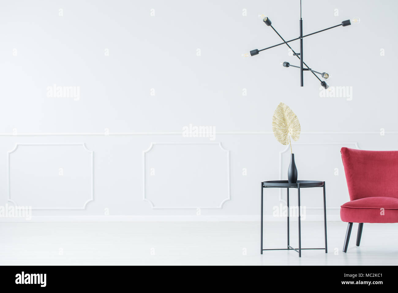 Semplice, stanza vuota con poltrona rossa, tabella con un vaso su di essa e una lampada Foto Stock