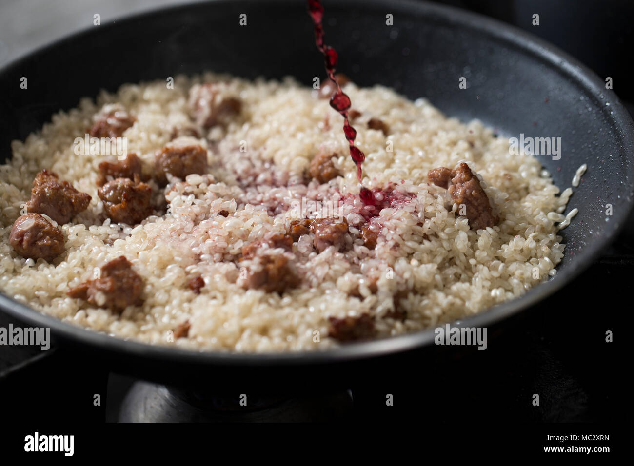 Primo piano di una pentola piena di riso con salsicce e vino rosso, lo chef è versando il vino rosso in padella durante la cottura risotto italiano. Foto Stock