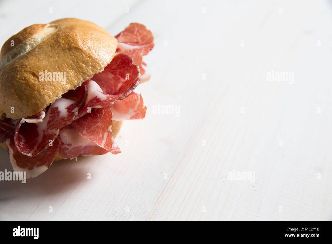 Tipica italiana con sandwich coppa ( fatta a Piacenza, Italia del nord) su un bianco tavolo di legno, oggetto di un focus sulla sinistra Foto Stock