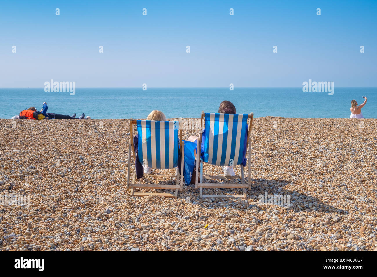 BRIGHTON, Regno Unito - 8 Aprile 2017: giovane seduto in sedie a sdraio su un soleggiato aprile giornata sulla spiaggia di Brighton in aprile 2017. Foto Stock