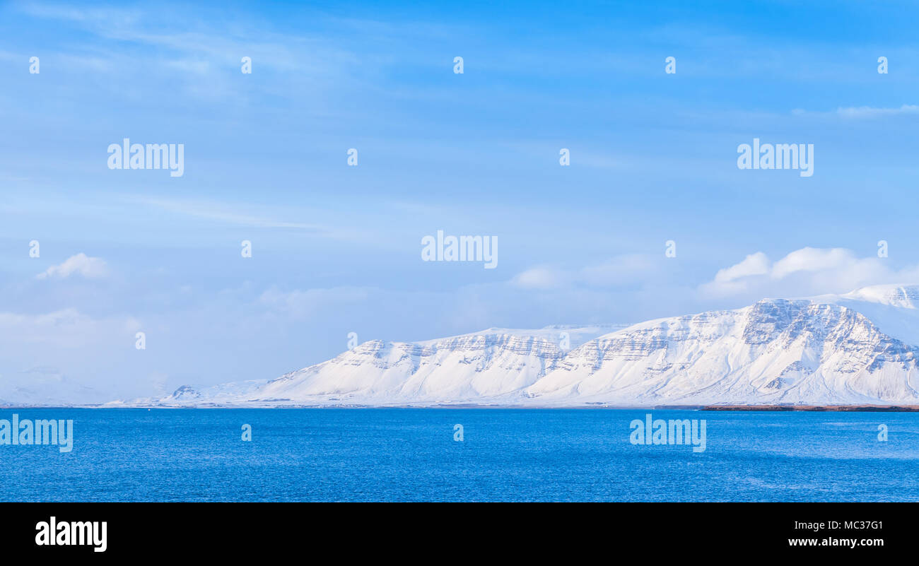 Islandese il paesaggio costiero, montagne innevate sull orizzonte sotto il cielo blu. Reykjavik, Islanda Foto Stock