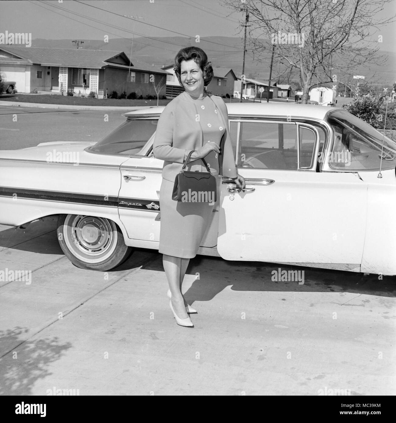 Un felice donna matura si distingue per la sua Chevy Impala auto in California, ca. 1965. Foto Stock