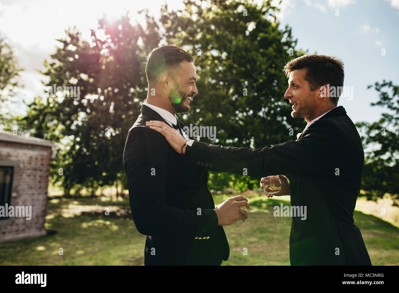 Lo sposo di parlare con il suo uomo migliore con drink in mano durante la festa di nozze. Lo sposo e groomsmen festa dopo il matrimonio al Park. Foto Stock