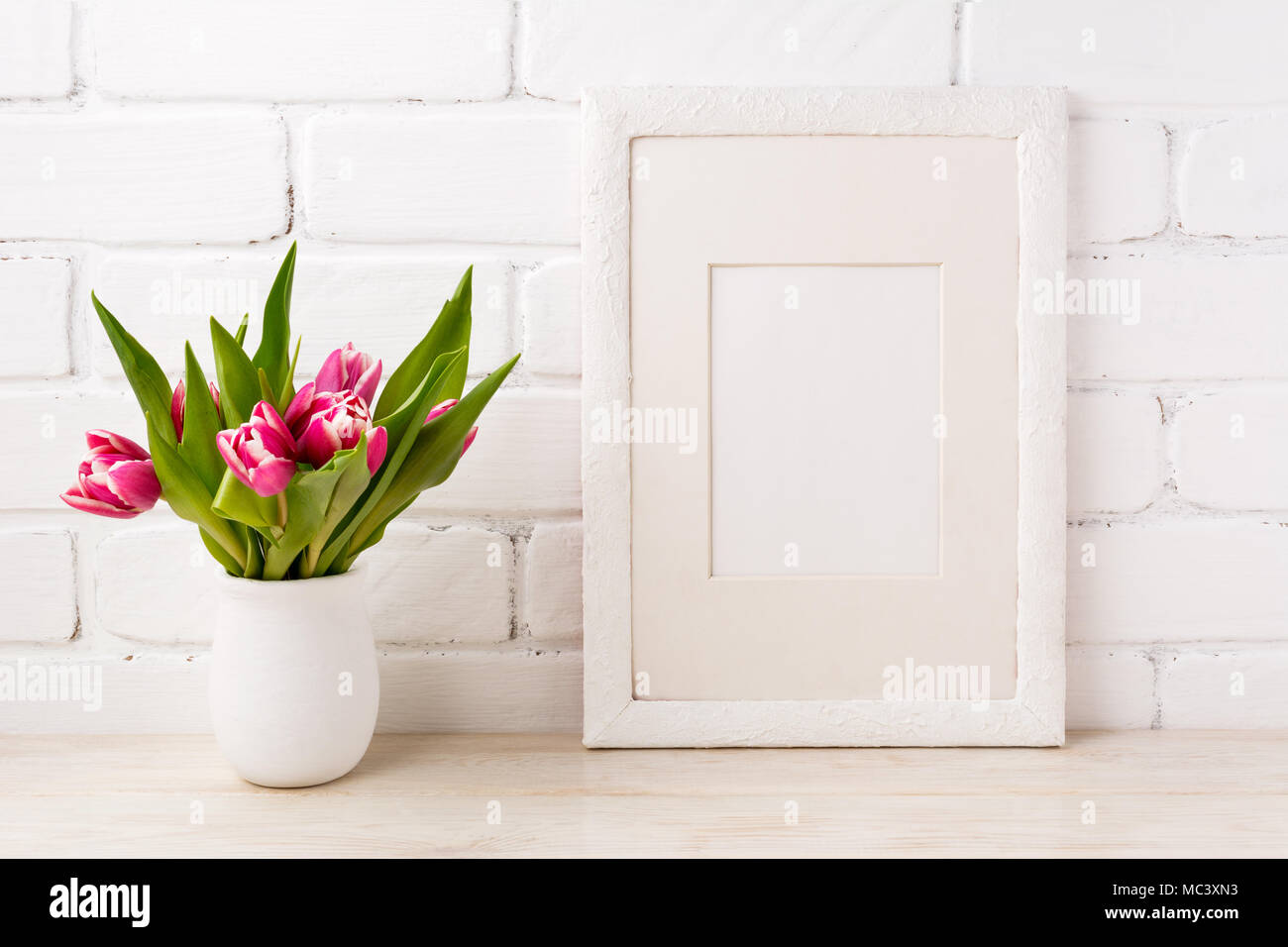 Cornice bianca mockup con luminosi di colore rosa magenta tulip bouquet in vaso di fiori. Fotogramma vuoto mock up di presentazione di opere d'arte. Inquadratura del modello per le moderne Foto Stock