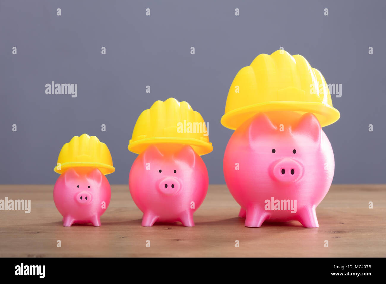 Close-up di crescente Rosa Piggy banche con Casco giallo sulla scrivania in legno Foto Stock