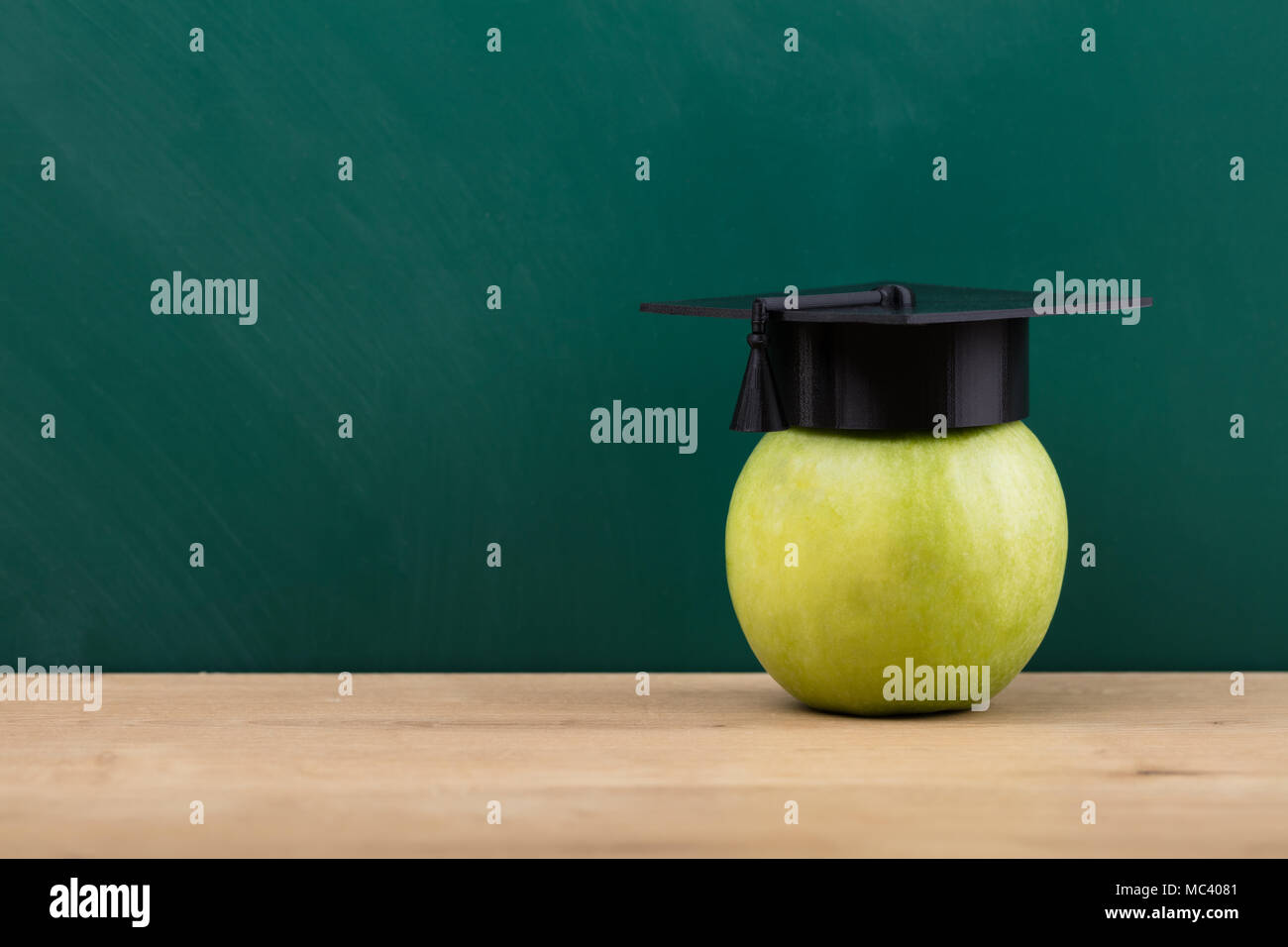 Close-up di una mela verde con graduazione Hat sulla scrivania in legno Foto Stock
