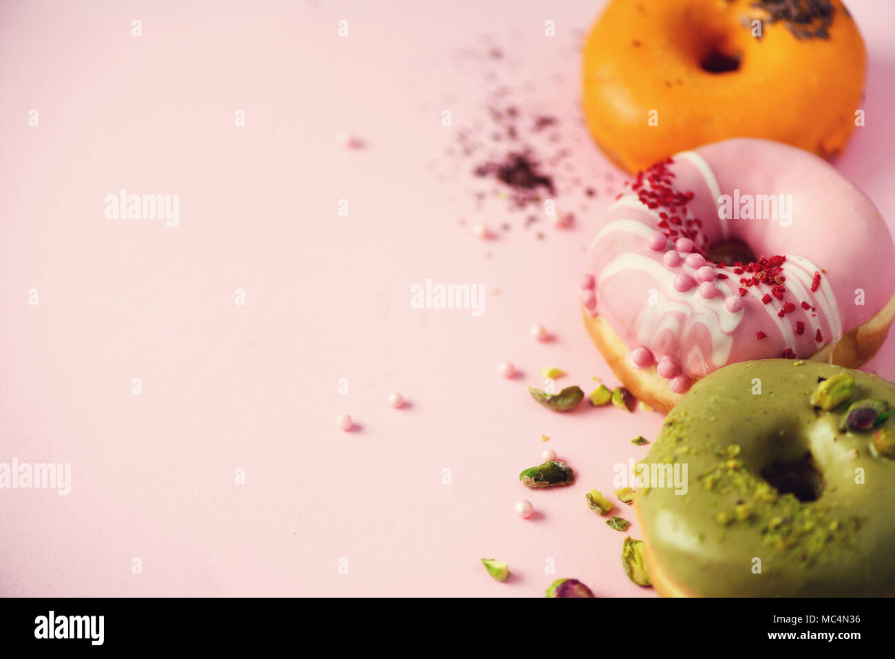 Ciambelle colorate con ciliegina sulla rosa pastello sfondo. Arancio dolce, verde, rosa ciambelle con pistacchio, cioccolato. Appartamento laico, vista dall'alto, spazio di copia Foto Stock