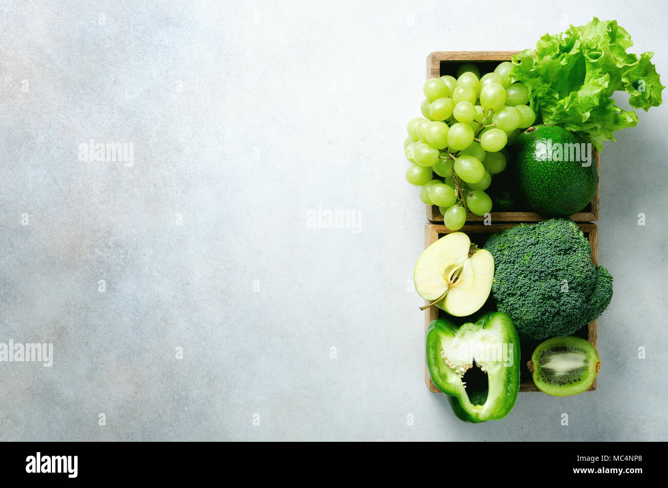 Verde biologico di frutta e verdura su sfondo grigio. Spazio di copia, piatto di laici che, vista dall'alto. Verde mela, lattuga, zucchini, cetrioli, avocado, kale, calce, kiwi, uva, banana, broccoli Foto Stock