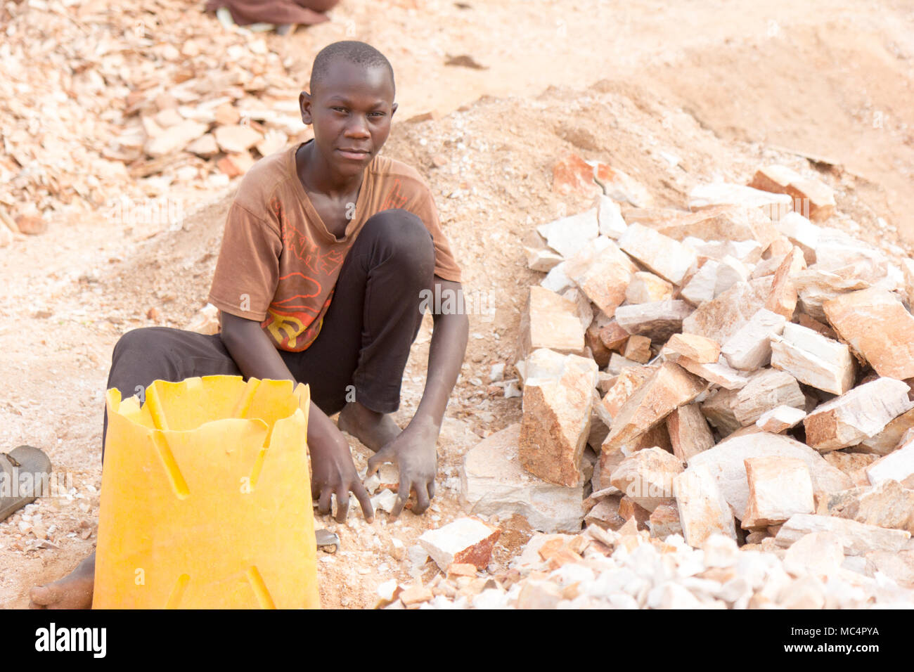Lugazi, Uganda. Il 18 giugno 2017. Un ragazzo ugandese rocce di rottura in lastre di piccole dimensioni per il suo caposquadra. In sostanza il lavoro minorile. Foto Stock