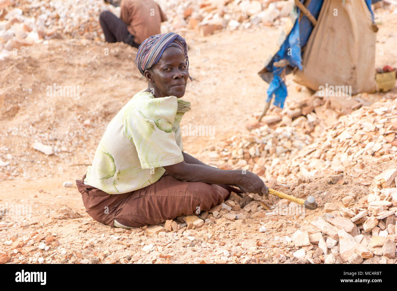 Lugazi, Uganda. Il 18 giugno 2017. Una donna ugandese rocce di rottura in lastre di piccole dimensioni per il suo caposquadra. Foto Stock