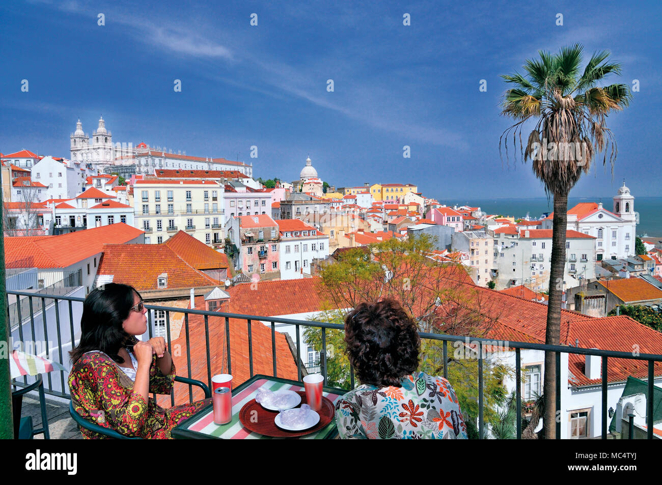 Due donne gustando bibite sulla terrazza soleggiata con vista di Lisbona Foto Stock