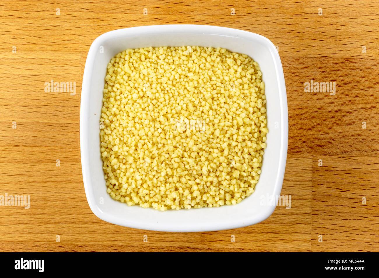 Tettuccio di colpo di couscous crudo in una ciotola bianco su uno sfondo di legno Foto Stock