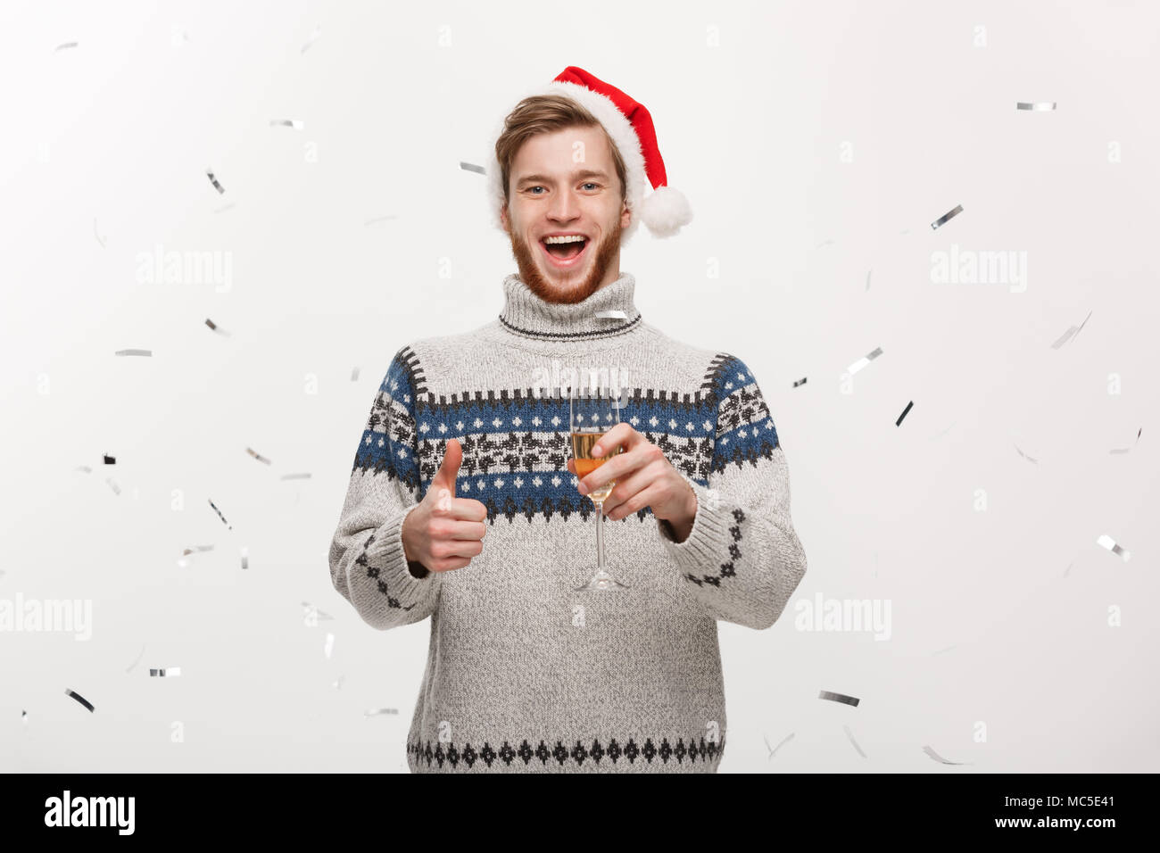 Concetto di natale - Happy giovani caucasici uomo barba holding champagne vetro con sfondo di confetti per celebrare il giorno di Natale. Foto Stock