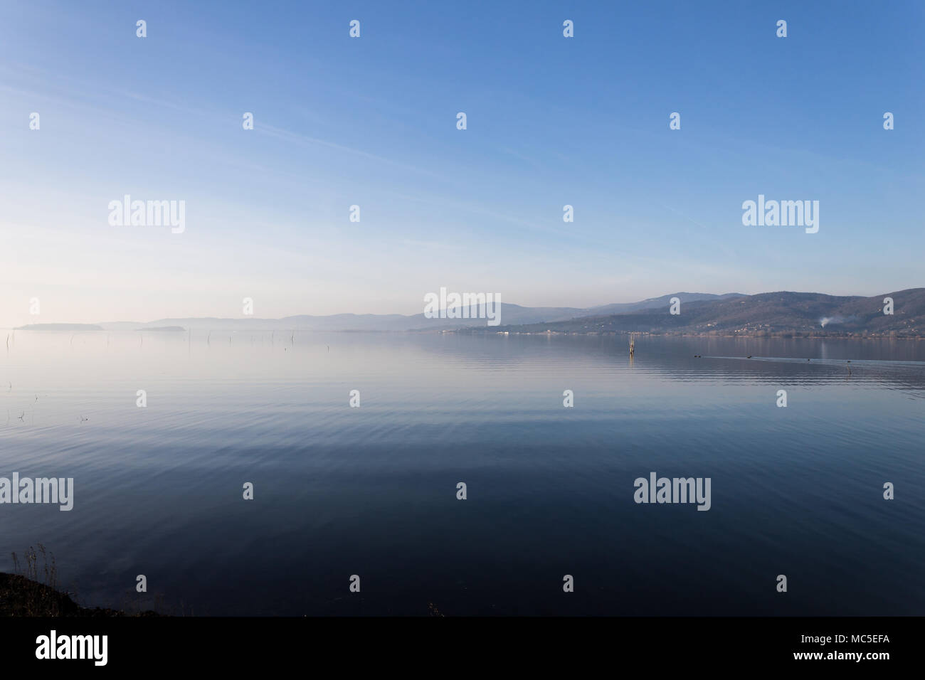 Bellissima vista del lago Trasimeno (Umbria, Italia), con colline e cielo blu che riflette sull'acqua Foto Stock