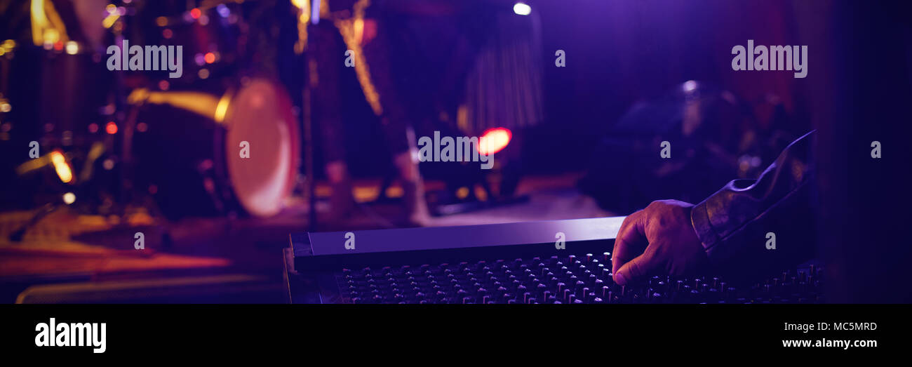 Uomo di funzionamento mixer audio con la partecipazione di musicisti sul palco illuminato in discoteca Foto Stock