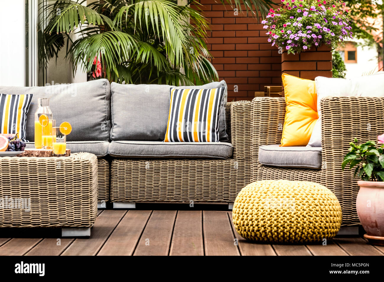 Pouf giallo accanto a una poltrona di rattan sulla terrazza in legno con  cuscini a strisce sul divano Foto stock - Alamy