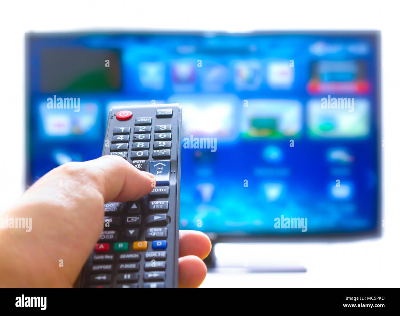 Mano, premendo sul telecomando e cambia i canali il pollice sul blu sullo schermo TV Foto Stock