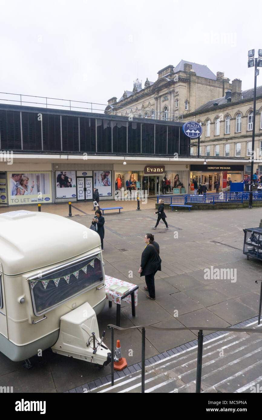 Area commerciale urbana con una piazza pedonale, negozi e roulotte parcheggiate: Un'istantanea della vita quotidiana della città Foto Stock
