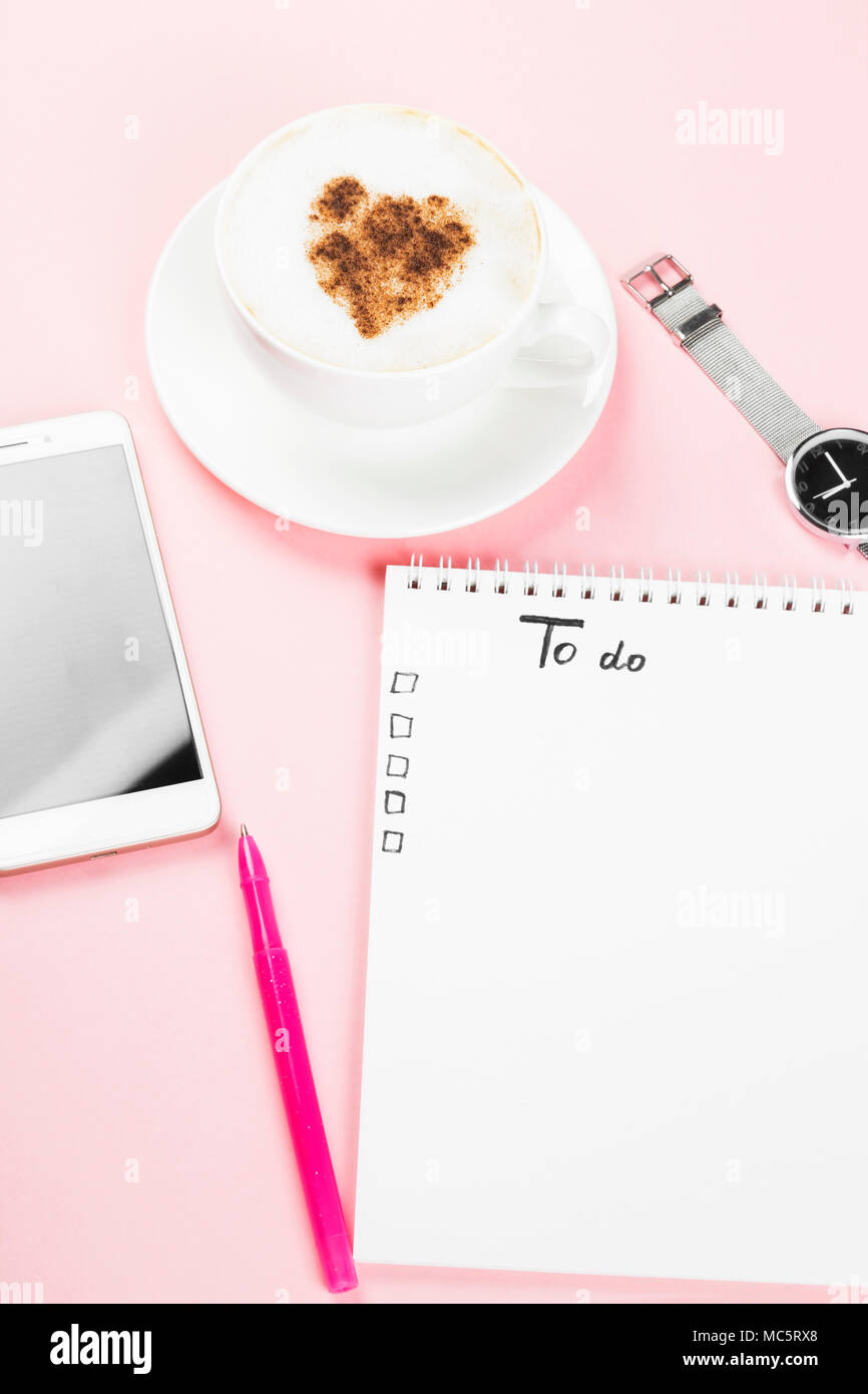 Il concetto di pianificazione mattino, lista Da fare - cappuccino, notebook, penna, telefono, guarda su sfondo rosa. Spazio di copia Foto Stock