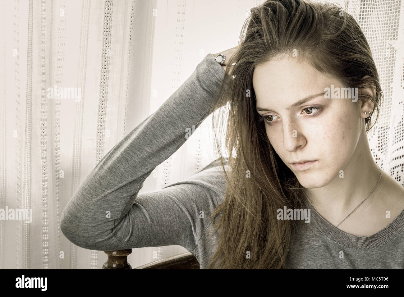 Adolescente ragazza seduta a casa con la sua mano sulla testa guardando verso il basso pensando. Foto Stock