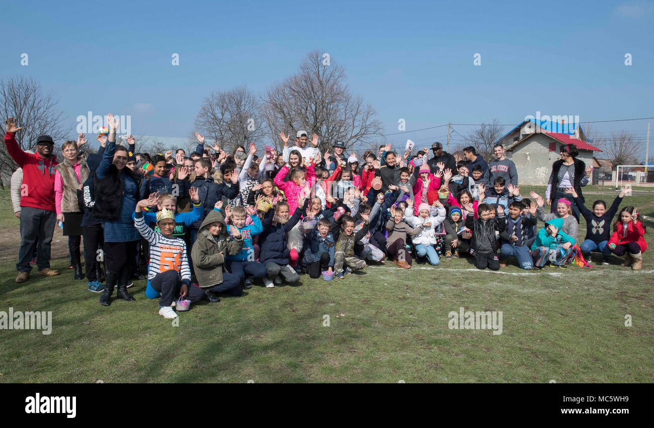 DEVESELU, Romania (28 marzo 2018) i marinai e i civili dalla base navale di meccanismo di sostegno Deveselu scattare una foto di gruppo con gli amministratori delle scuole e bambini dalla scuola Deveselu, una locale scuola rumena, durante un uovo di Pasqua le relazioni tra comunità (COMREL) progetto. NSF Deveselu AAMDS e Romania sono co-localizzato con il rumeno 99th Base Militare e gioca un ruolo chiave nel missile balistico di difesa in Europa orientale. Foto Stock