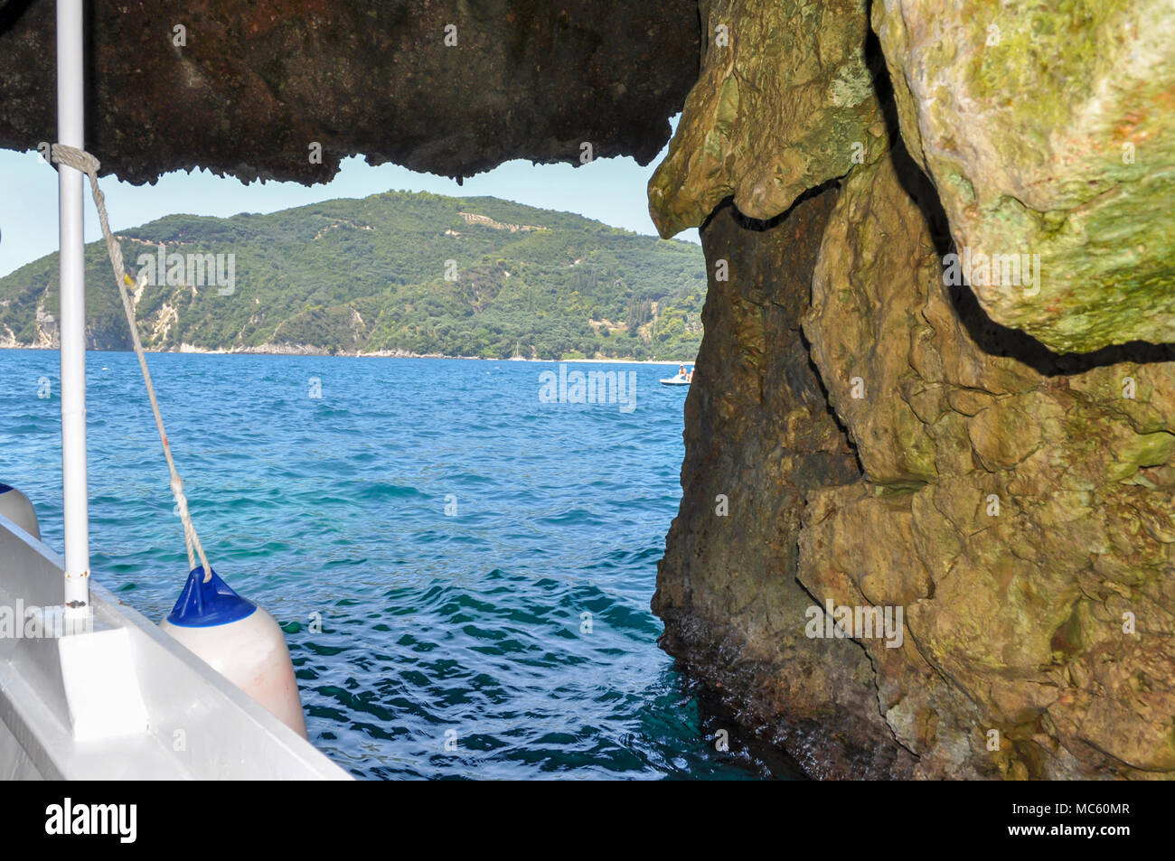 Parga, Epiro - Grecia. Uscendo da una grotta marina per la zona di mare di Parga con la barca tradizionale di un uomo nativo che organizza visite guidate del mare. Giornata di sole Foto Stock