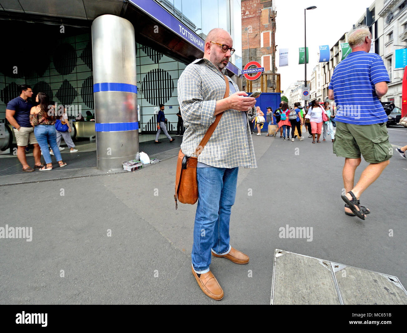 Londra, Inghilterra, Regno Unito. L'uomo per il suo telefono cellulare fuori dalla fermata Tottenham Court Road della metropolitana Foto Stock
