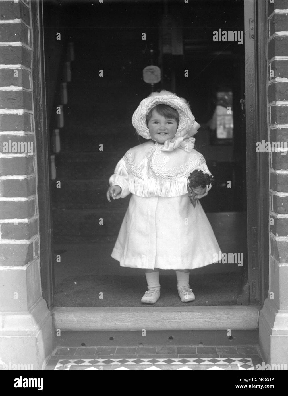 AJAXNETPHOTO. 1910 (circa). Posizione sconosciuta. - FAMILY SNAPSHOT - BAMBINO IN PIEDI NELLA PORTA IN BIANCO Abito in raso, Cape e cofano tenendo un POSY. fotografo:sconosciuto © IMMAGINE DIGITALE COPYRIGHT VINTAGE AJAX Picture Library Fonte: AJAX FOTO VINTAGE COLLEZIONE REF:181004 07 Foto Stock