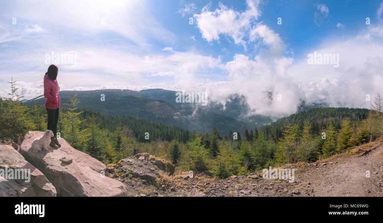 Bruna giovane donna con il suo cane su una roccia alta, ammirando la vista delle montagne e cloudscape nella Foresta Nera settentrionale, Germania. Foto Stock