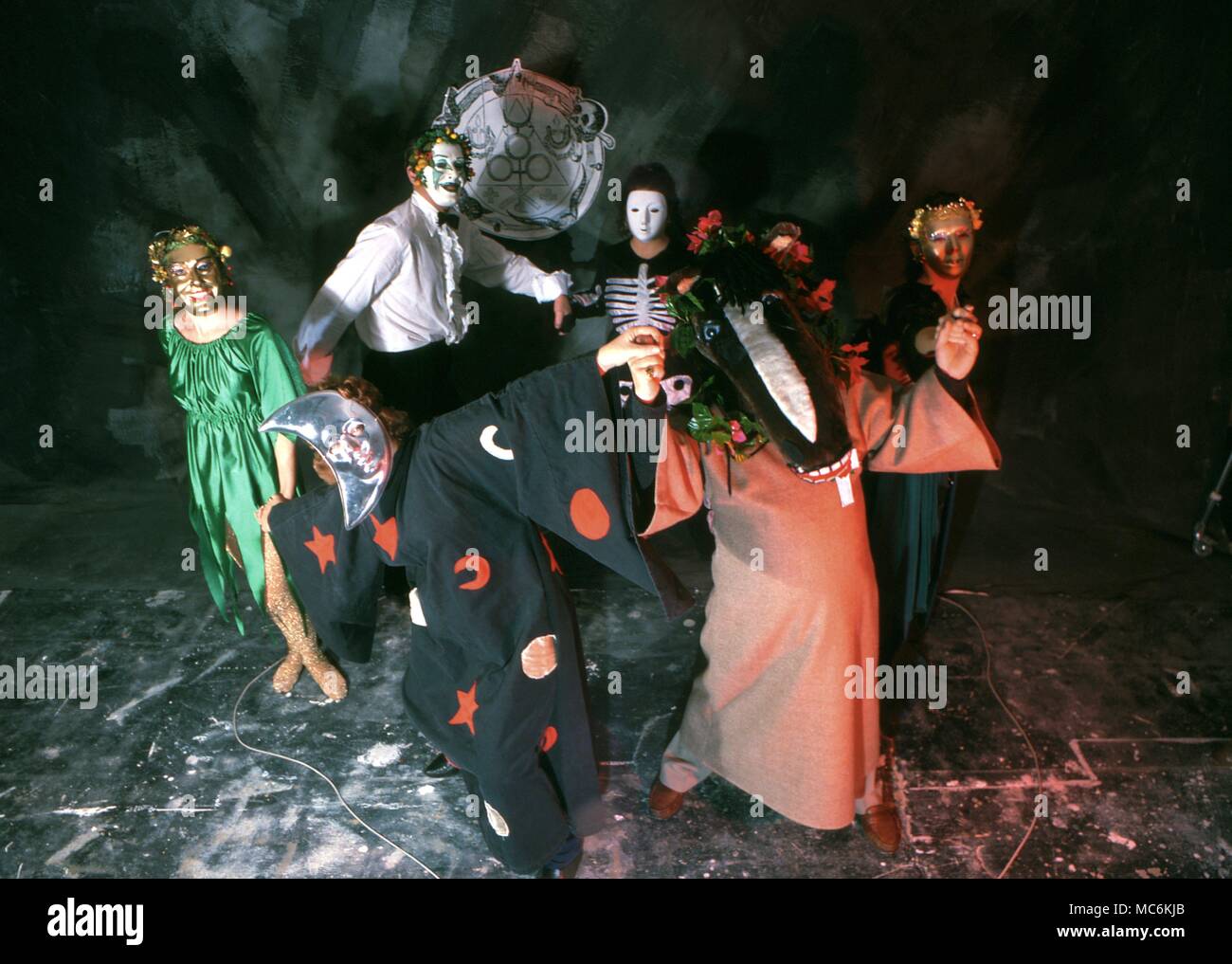 Un gruppo di persone in una stregoneria burlesque, vestito in costumi stravaganti e maschere, balli all'interno di un cerchio magico. Foto Stock