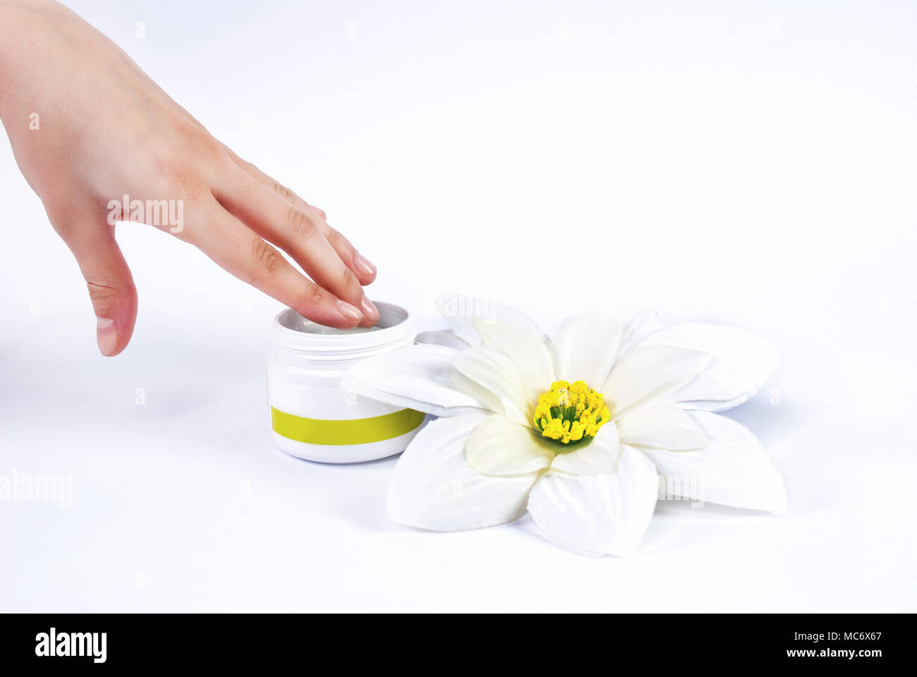 Donna mano mette il dito in una ciotola di crema per il viso e per il fiore bianco accanto box Foto Stock