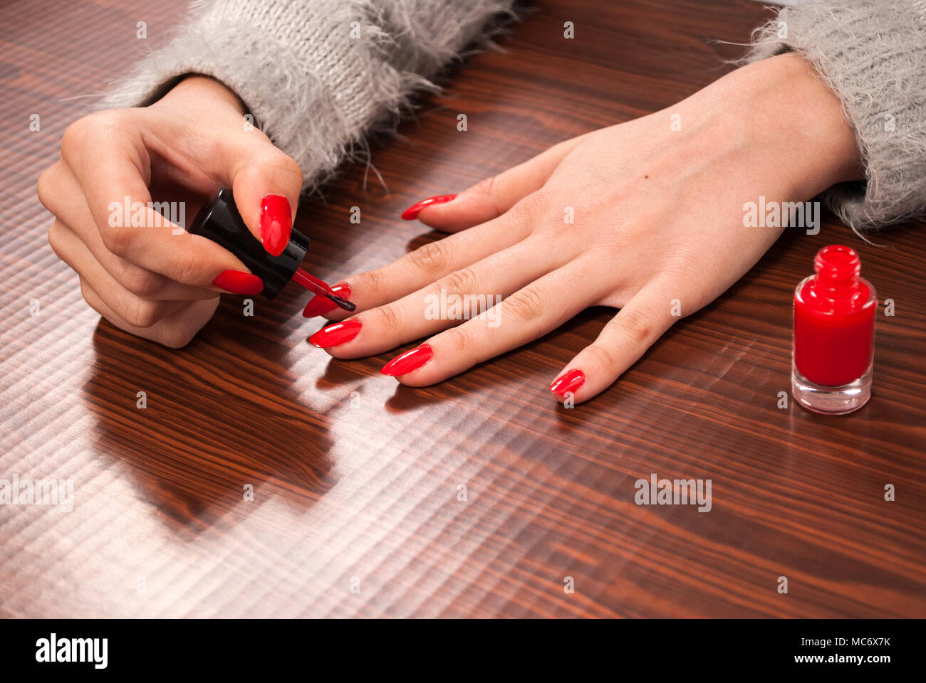 La donna la sua pittura chiodi sul dito di colore rosso sulla scrivania in legno Foto Stock