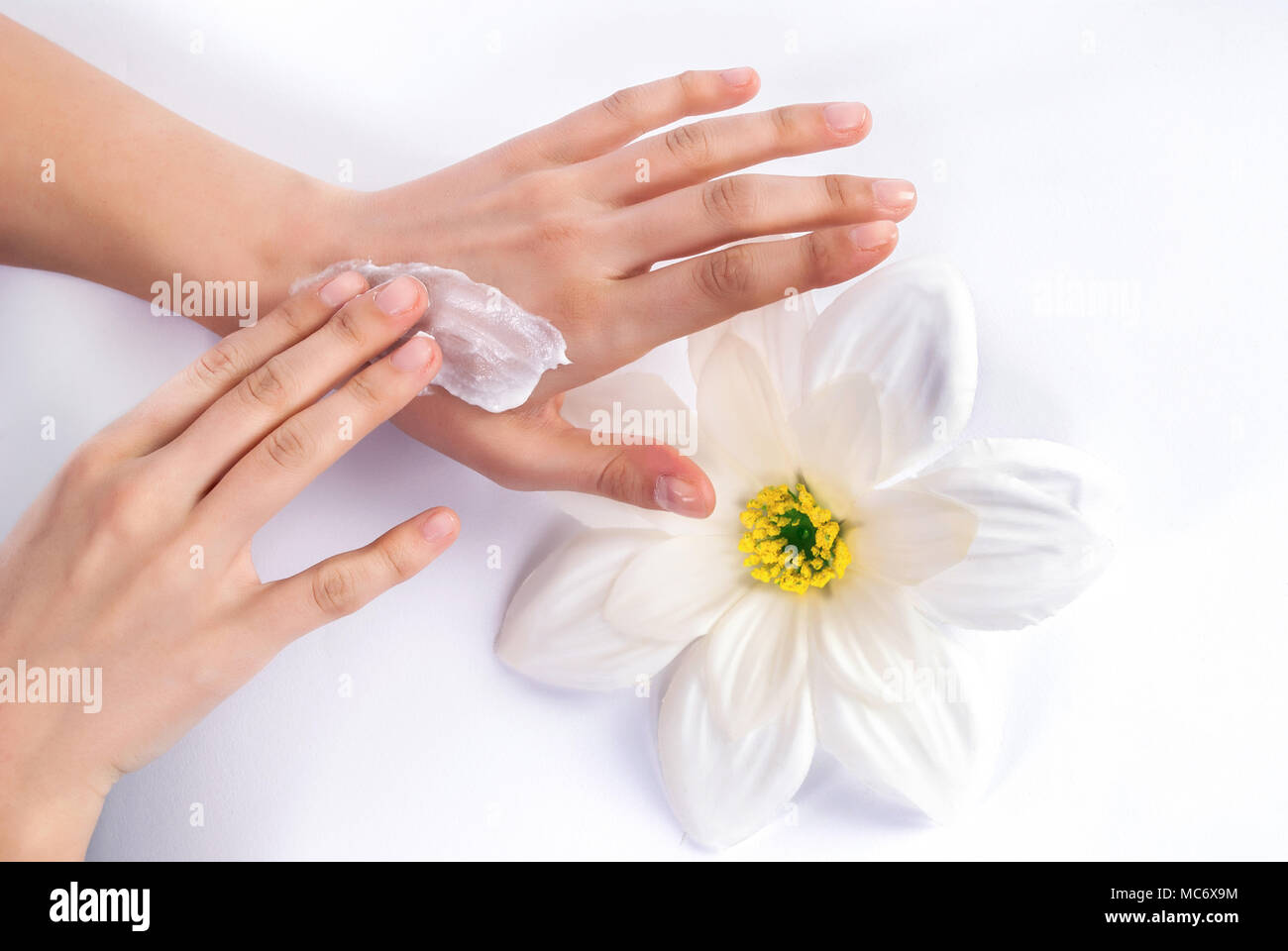 Giovane donna di applicare la crema su belli e curati mani e fiore bianco in background Foto Stock