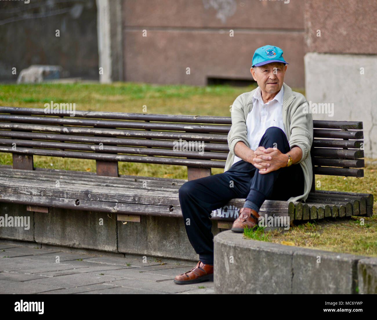 Un anziano uomo seduto su una panchina indossando un cappello da basket (Charlotte Hornets), Kaunas, Lituania Foto Stock