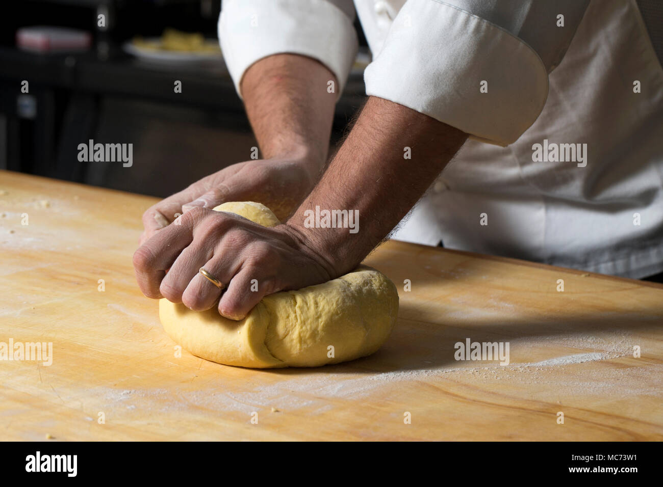 Un primo piano di un uomo impastando una palla di pasta fatta con farina e uova su una tavola di legno Foto Stock