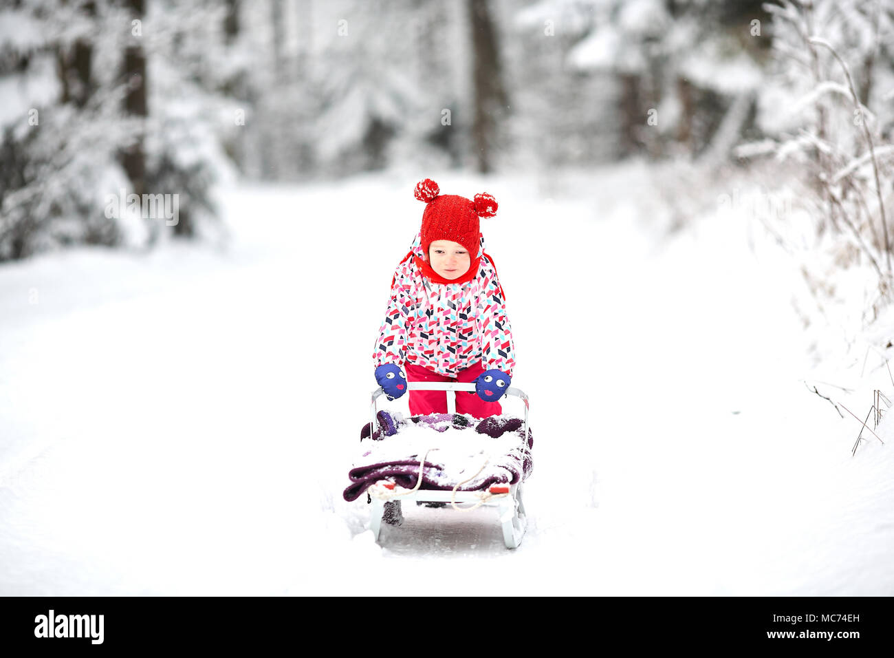 Giovane bella ragazza bambino creando e giocando contro un parco invernale e dello sfondo con la neve nella bella foresta. Slitta di traino Foto Stock