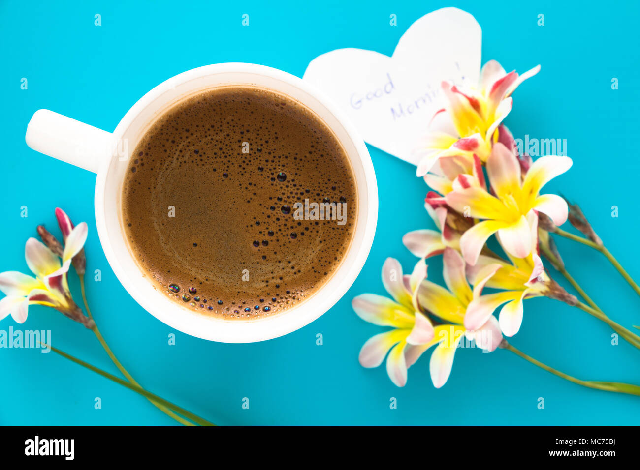Una tazza di caffè con fiori colorati e buona mattina nota, sulla superficie blu. Foto Stock