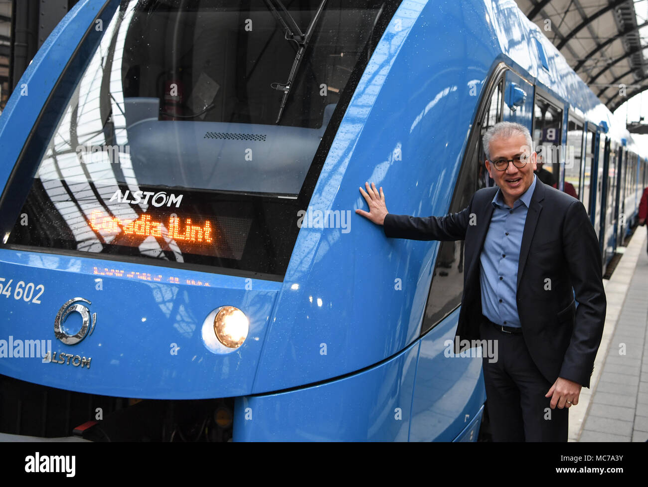 13 aprile 2018, Germania, Wiesbaden: di Hesse Economia e ministro dei Trasporti, Tarek Al-Wazir dell'Alleanza 90/Partito Verde sorge sulla piattaforma accanto ad una cella a combustibile alimentata a treno communter del costruttore francese Alstrom. Il trasporto regionale associazione 'Rhein-Main-Verkehrsverbund' vuole sostituire il treno diesel motori che sono stati la manutenzione di quattro non elettrificate linee secondarie nella regione Taunus. Foto: Arne Dedert/dpa Foto Stock