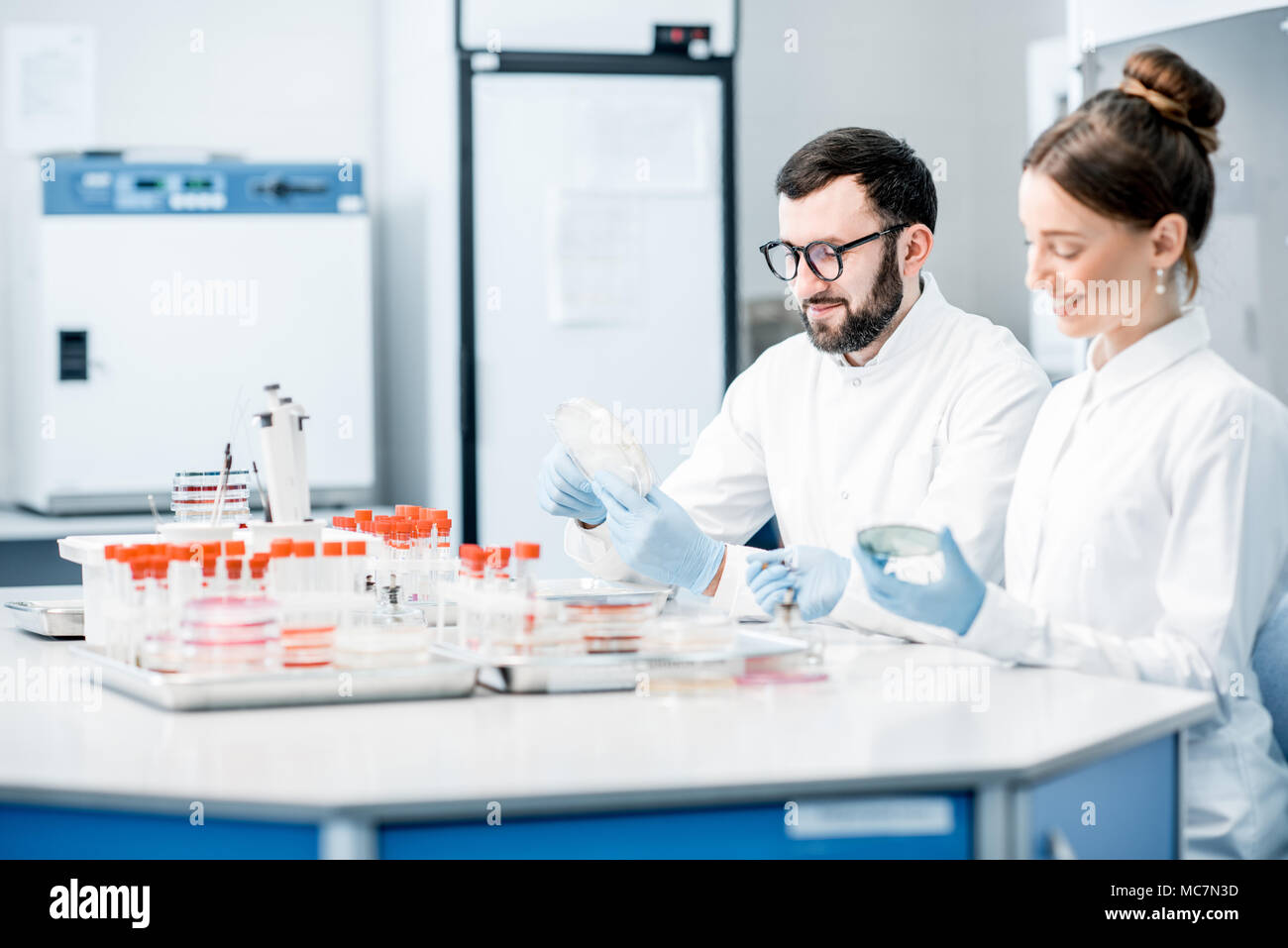 Paio di medici in uniforme facendo esami batteriologici in seduta il moderno laboratorio Foto Stock