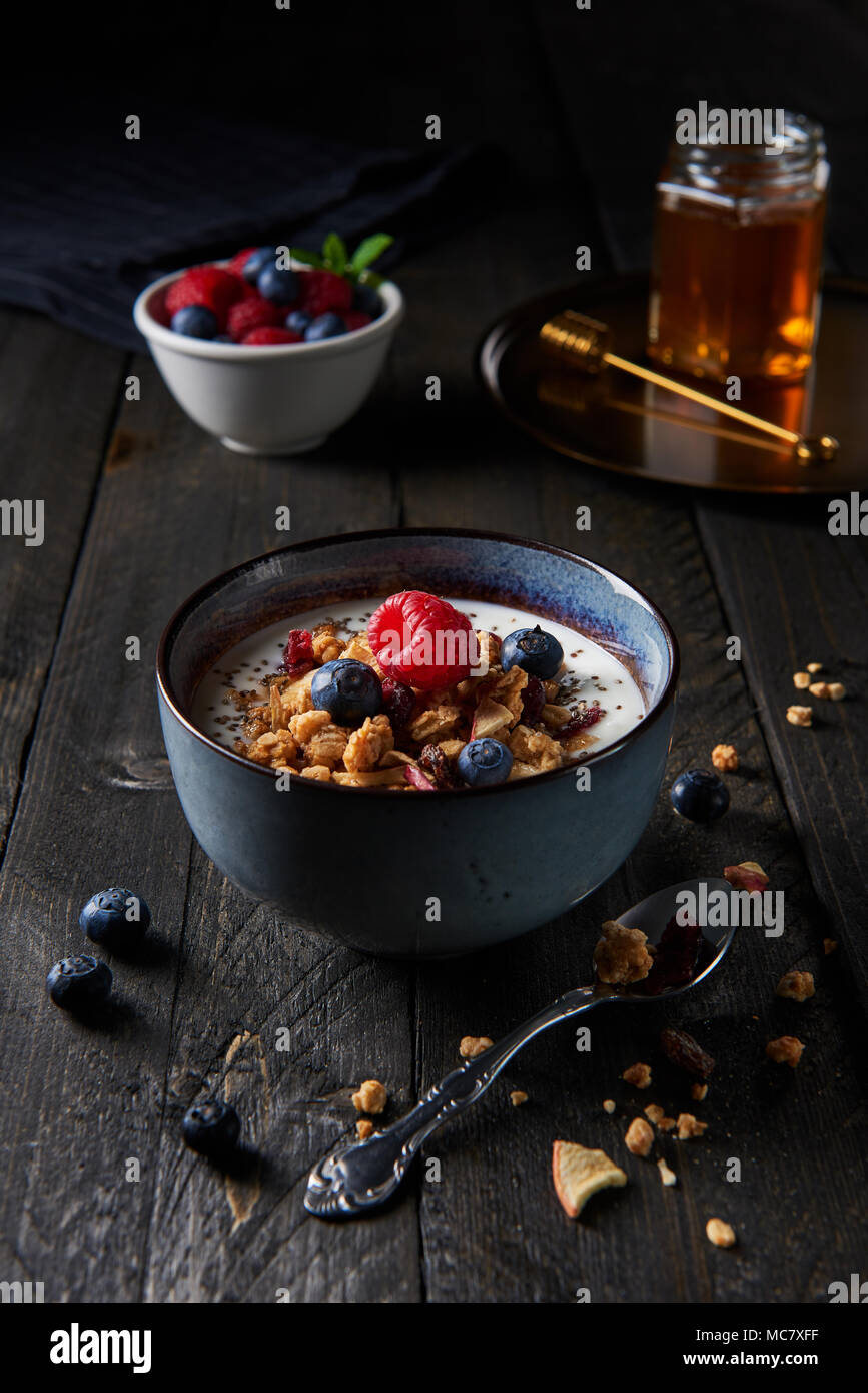 Il Granola fresca, muesli con yogurt, essiccato apple, mirtilli e lamponi e chia semi con miele e frutti di bosco misti in bianco ciotola di legno scuro. Foto Stock