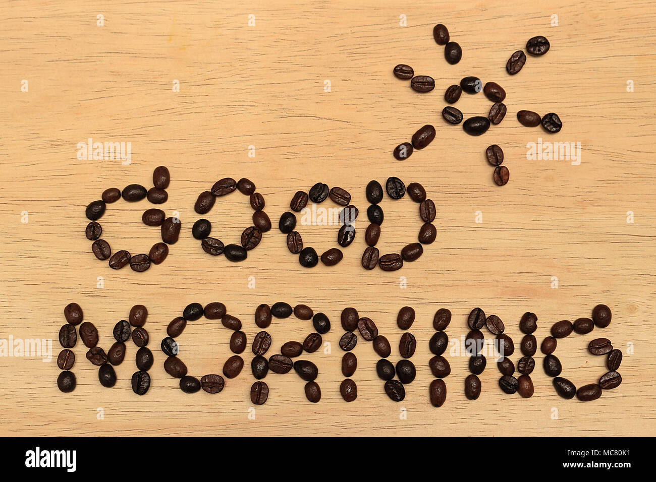 Vi è un messaggio 'good morning' e una foto del sole sopra il messaggio, tutto fatto di chicchi di caffè, lo sfondo è una tavola di legno. Foto Stock