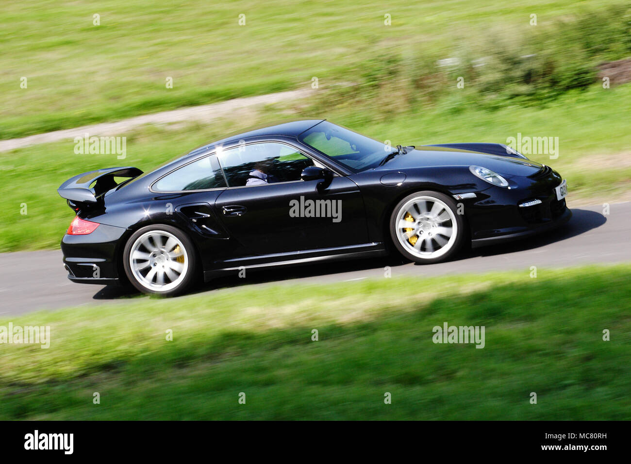 Profilo (vista laterale) di un nero Porsche 911 997 Turbo guida veloce su strada pubblica. Foto Stock