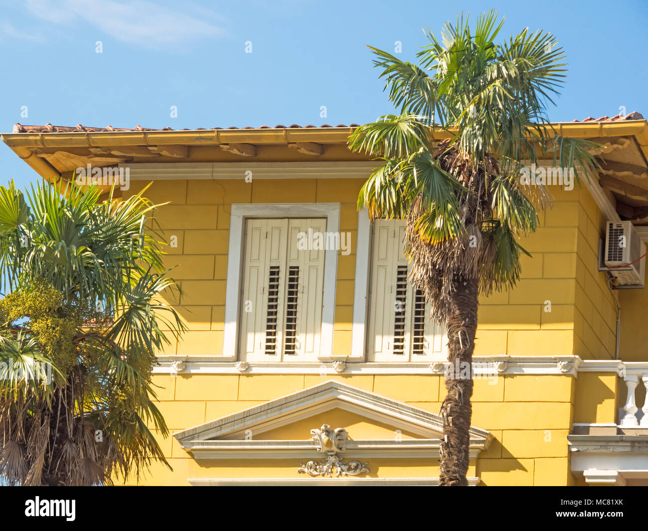 Il vecchio edificio giallo con palme in Lovran, Croazia Foto Stock