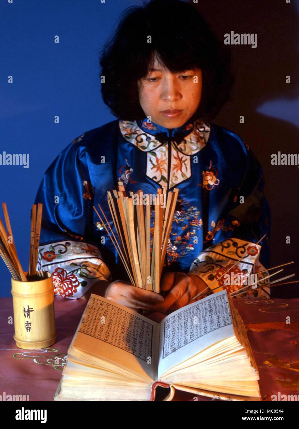 I Ching ragazza cinese di consultazione del testo sacro dell'I Ching, con bastoni, come richiesto nel sistema tradizionale Foto Stock