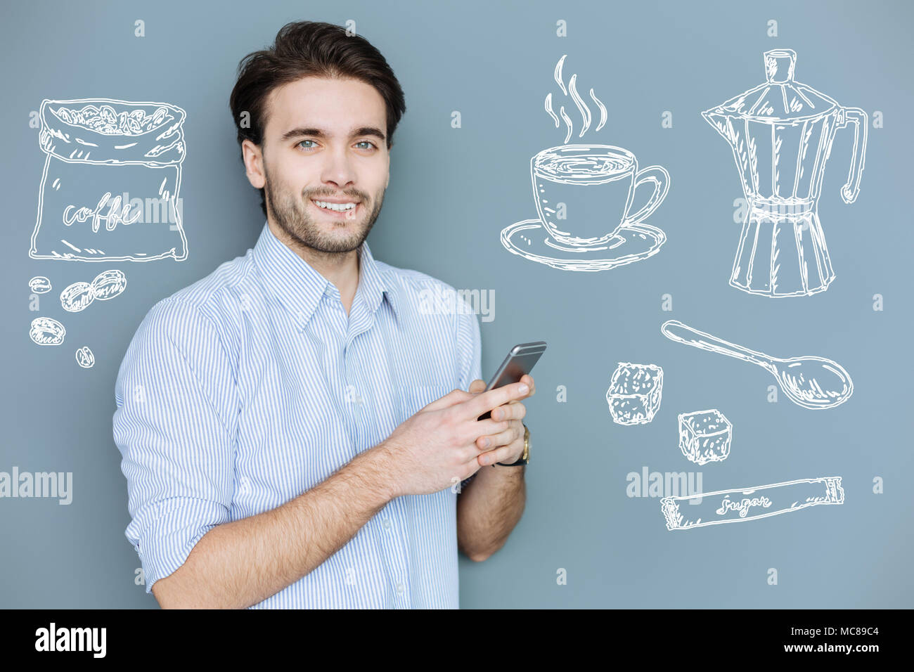 Sorridente manager tenendo un smartphone e pensando a bere il caffè Foto Stock