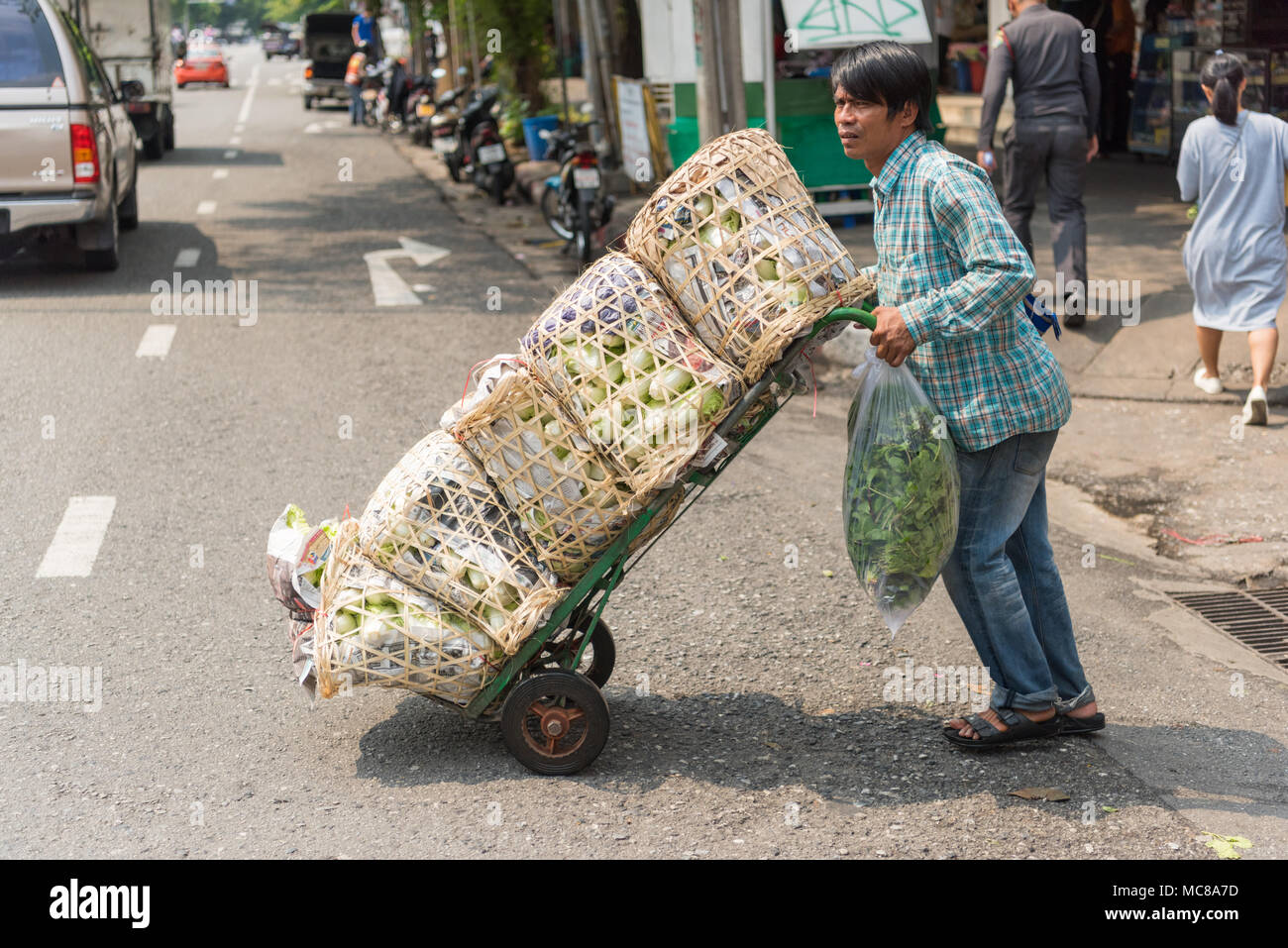 Un lavoratore in Bangkok di mercato dei fiori spinge produrre merci e su un sacco di Barrow Foto Stock